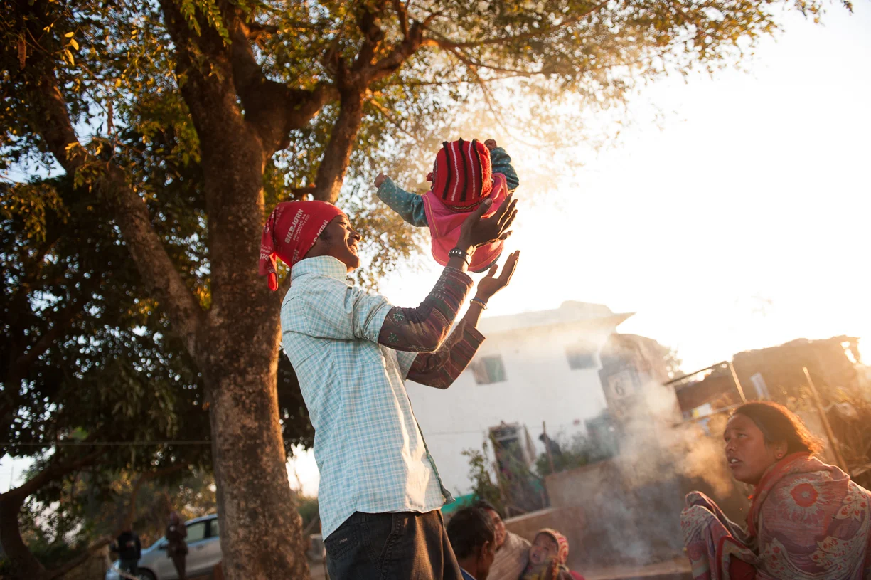 Mother looks on angrily as the young man playful tosses her baby into the air.