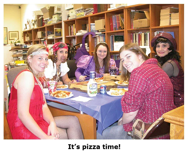 Costumed staffers at the coin shop eat pizza