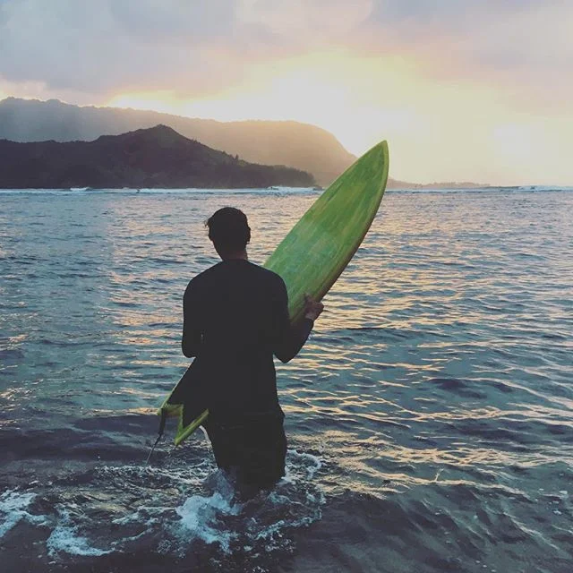 A handsome surfer paddles out to the surf break at sunset in Hanalei Bay on Kauai, Hawaii –– where Laird Hamilton resides.  
