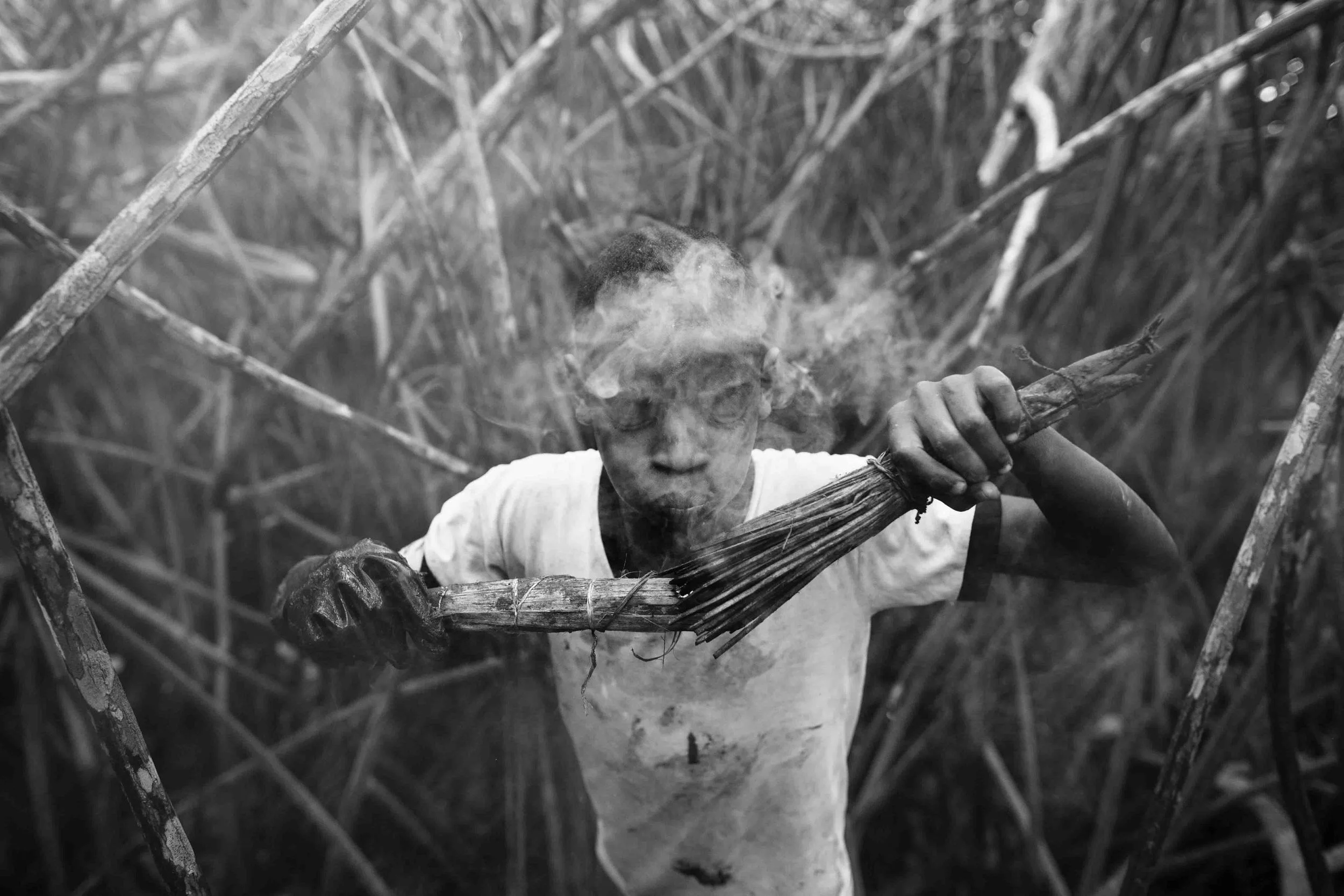 Jefferson Muñoz lights blows into a torch made out of coconut husks. The torches blow smoke for hours repelling the vicious mosquitoes and black flies of the mangrove. Bug spray only repels insects for a few minutes after application. 2014.