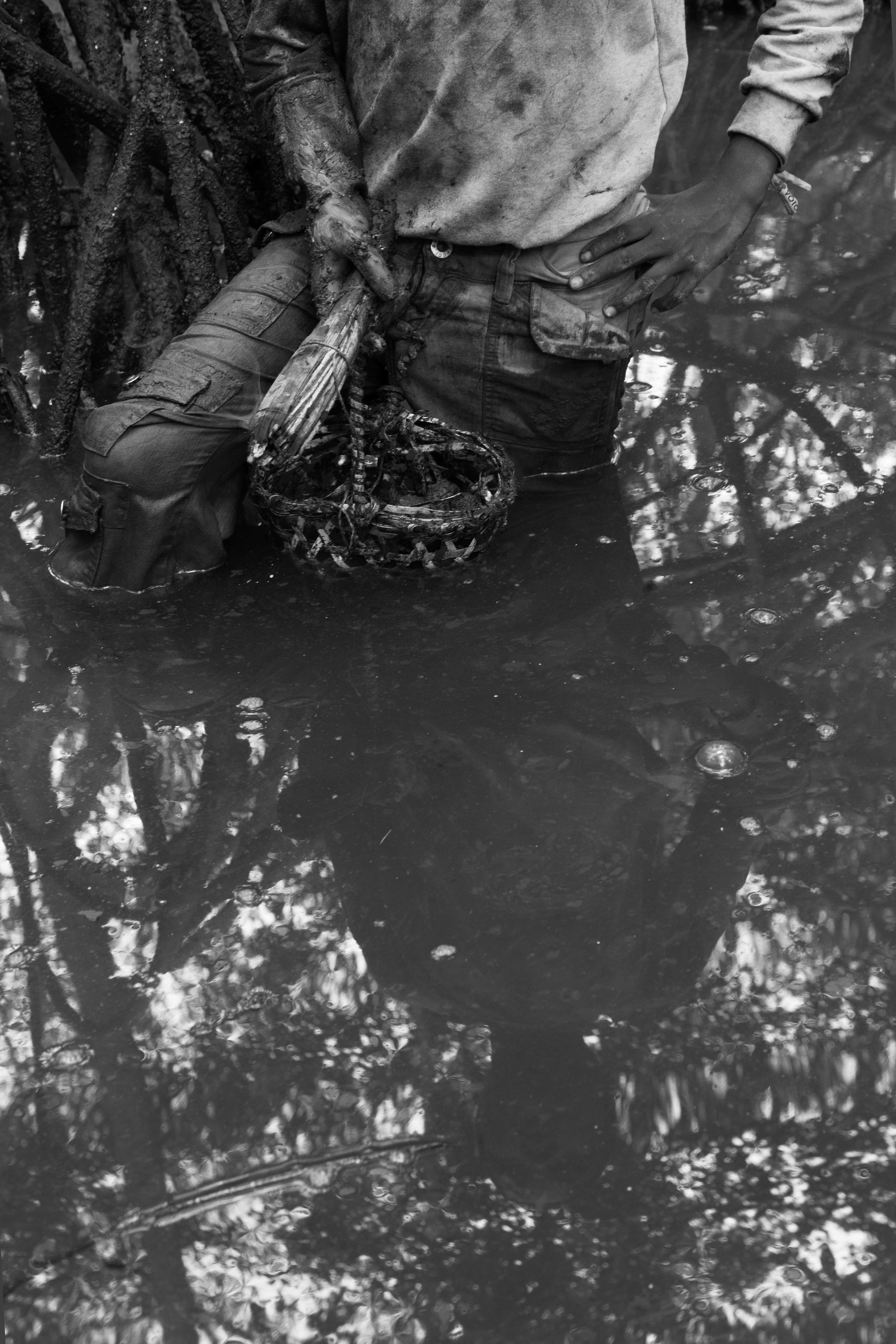  The reflection of Diego Reasco holding his basket and torch can be seen in the water of the Cayapas Mataje Mangrove Reserve. Work days in the mangrove are determined by the ebb and flow of the water. 2014. 