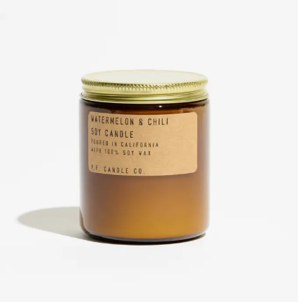 An amber glass candle jar featuring a kraft label and a brass lid, showcasing the Watermelon & Chili fragrance by P.F. Candle Co.