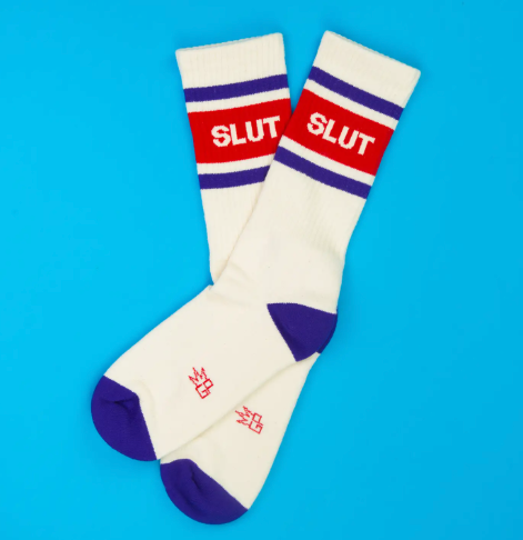 Showcase your style with American-made statement socks displaying solid purple heel and toe caps, a wide ribbed top, and crisp white block text graphics across the leg.
