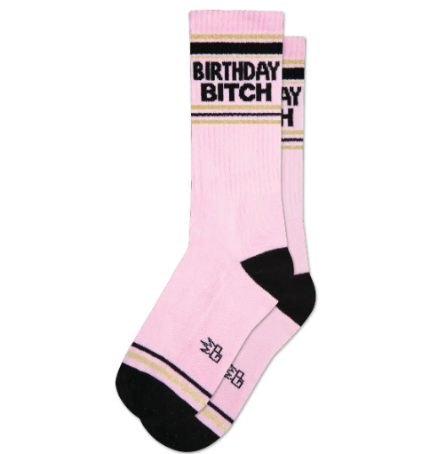 Declare your special day with the Gumball Poodle "Birthday Bitch" Gym Crew Socks, featuring bold gold and black lettering on a vibrant pink background, perfect for celebrating.