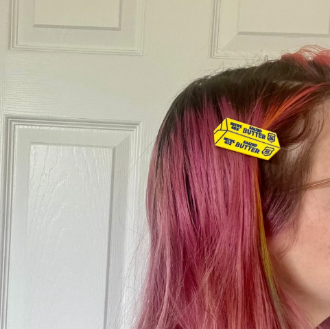 A person with pink hair wearing the yellow Boogie Bee Butter Flat Clip, showing how the clip sits securely on the side of the head as a statement accessory.
