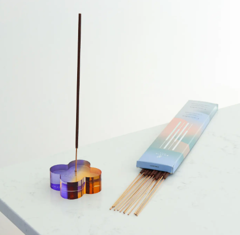 The Daisy Duotone Acrylic Incense Holder, a clover shape with a purple and orange gradient, holding an incense stick.