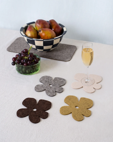 Style your dining table with the Merino Wool Fleurcoaster 4 Pack by Graf Lantz, shown supporting a wine glass alongside fruit and a serving bowl.