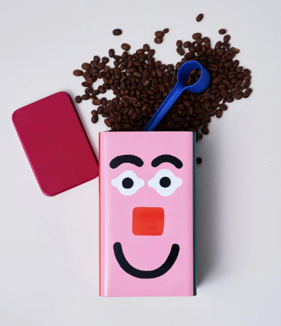 A stylish kitchen storage tin featuring a whimsical colorful faces pattern and a cobalt blue scoop.