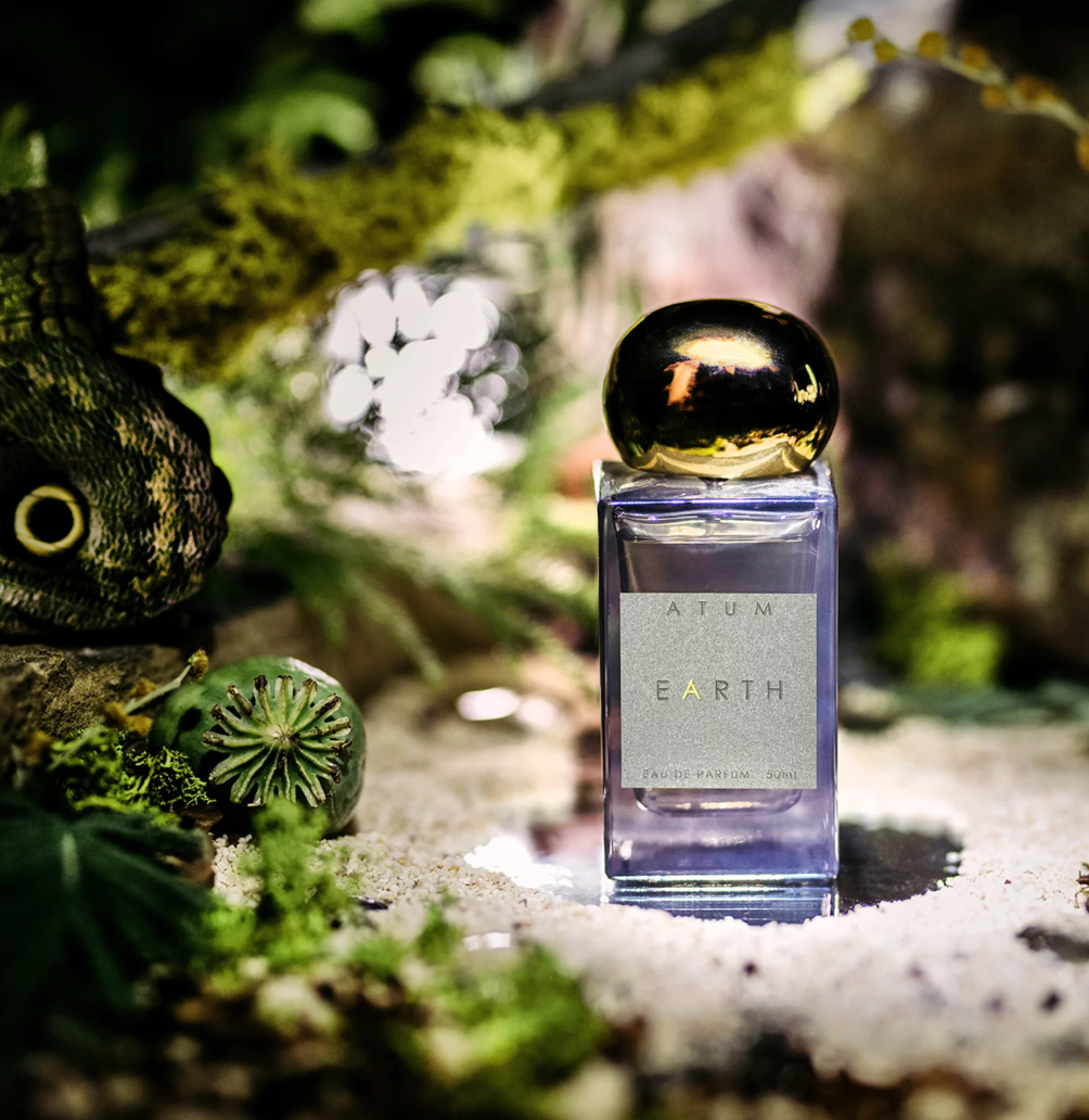 Earth Parfum by ATUM: The tinted grey glass bottle with a gold cap, beautifully illuminated in the forest, highlighting the fragrance's natural and luxurious essence.