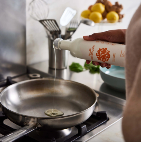 Pour chef-grade Algae Cooking Oil by Algae Cooking Club into a stainless steel skillet for high-heat cooking.
