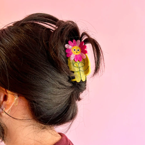 A whimsical flower-shaped hair claw featuring a cute sifaka lemur character in shades of orange and cream by The Peach Fuzz.