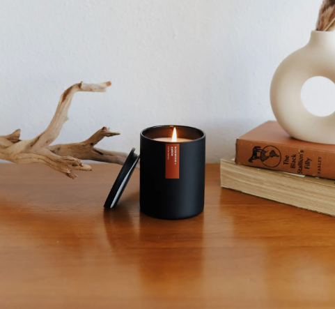 A beautifully lit Rosewood + Amber soy candle, showing its warm glow and sleek matte black tumbler, perfect for creating a peaceful atmosphere.