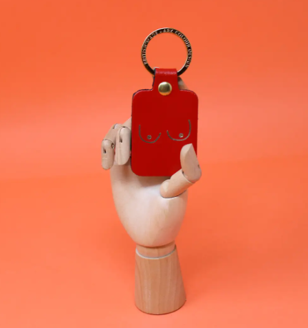 A unique and empowering red leather keyring shaped like a boob, a playful symbol of strength and femininity.