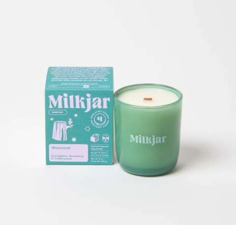 The Milkjar Woodland candle in a green glass jar next to its teal box, showing the eucalyptus scent profile.