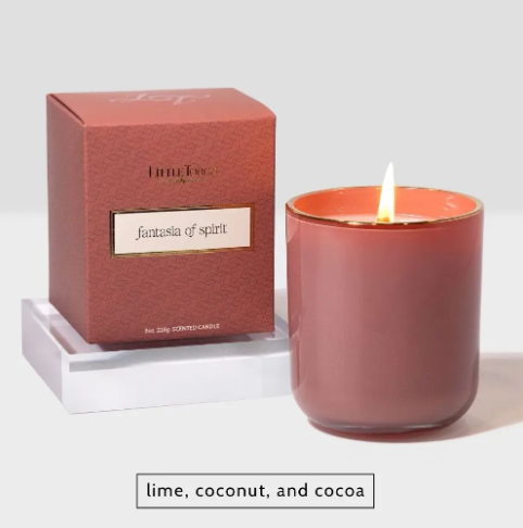 The Little Torch Fantasia of Spirit candle features a dusty rose vessel and matching box, glowing warmly with a lit wick, showcasing a fragrance inspired by self-discovery.