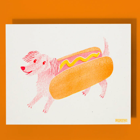 A whimsical risograph print of an adorable dachshund in a hot dog costume, perfect for adding a fun and quirky touch to any wall.