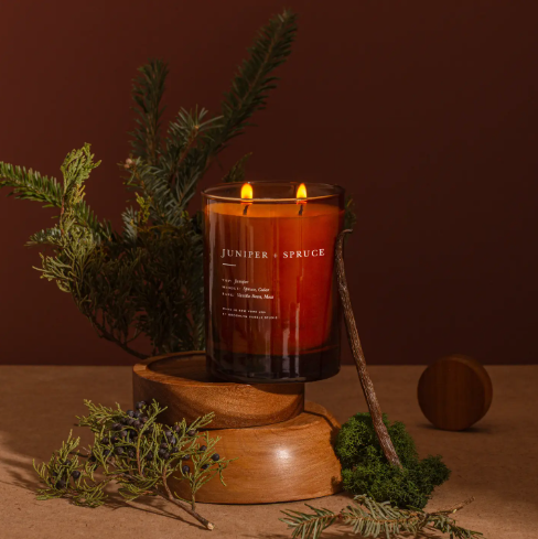 Create a cozy atmosphere with the lit Juniper and Spruce Candle by Brooklyn Candle Studio, styled with natural cedar and vanilla elements.