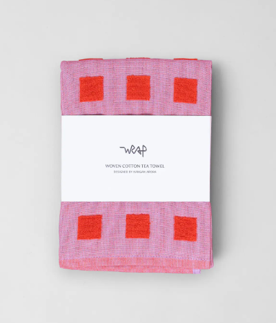 A folded Squares Cotton Tea Towel by Wrap in the Lilac/Warm Red colorway, showing a pattern of alternating light lilac and warm red squares.