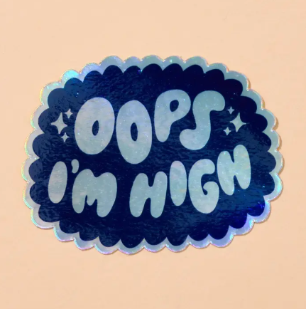 A close-up view of the holographic Oops I'm High die-cut vinyl sticker by And Here We Are, showcasing its sparkling finish and bubble lettering.