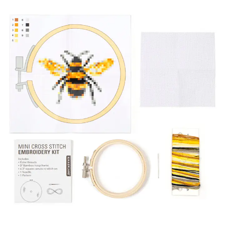 A complete kit layout showing the bamboo hoop, white fabric, colorful embroidery floss, and a bee pattern guide for a DIY project.