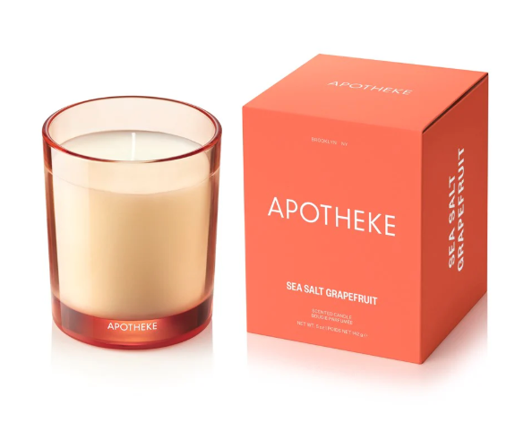 The APOTHEKE Sea Salt Grapefruit candle and its packaging, highlighting the warm, citrusy color of both the glass vessel and the minimalist box design.