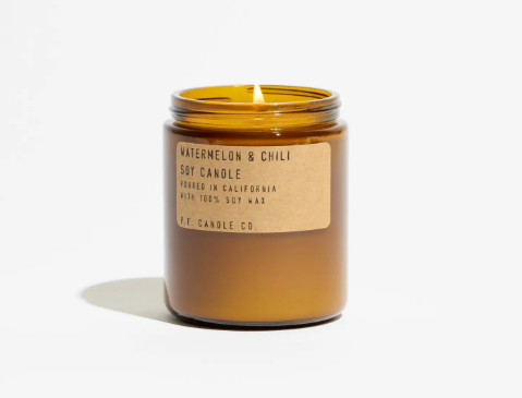 A lit amber glass soy candle casting a warm, inviting glow and filling your space with a joyful summer scent.