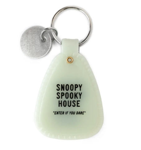 Display the back of the glow-in-the-dark Snoopy Mummy Saddle Keychain by Three Potato Four, stamped with a playful spooky house graphic.