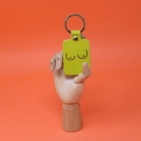 A unique and empowering acid green leather keyring shaped like a boob, a playful symbol of strength and femininity.