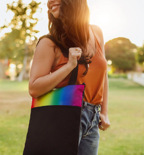 A model carrying the black tote bag with a striking rainbow band, suggesting outdoor use.