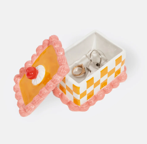 Store your rings and house keys inside a whimsical yellow and white checkered ceramic storage box featuring a realistic pink icing border and a red cherry handle.