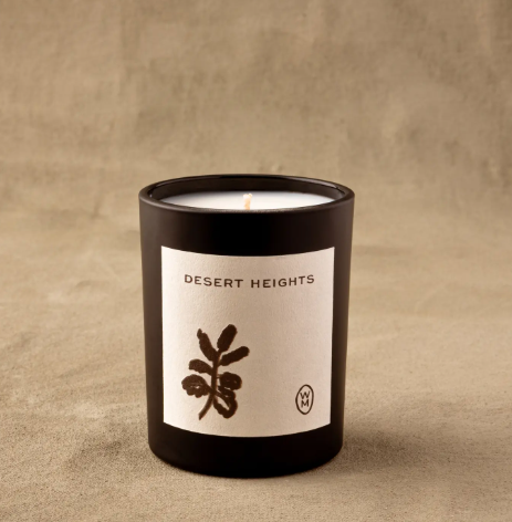 A single lit Desert Heights Luxury Candle by Wilkin & May casts a tranquil glow against a warm, neutral earth-toned backdrop.