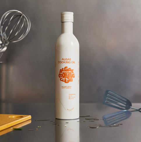 Showcase the sleek packaging of the Algae Cooking Oil by Algae Cooking Club, positioned on a kitchen counter with cooking utensils.