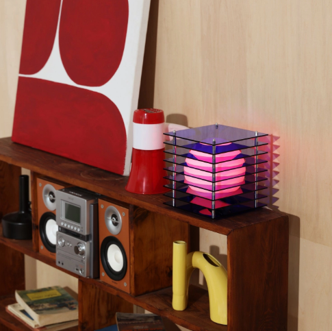 A blue LớP Small Square Light by BANG styled on a wooden shelf next to modern art pieces and retro speakers.
