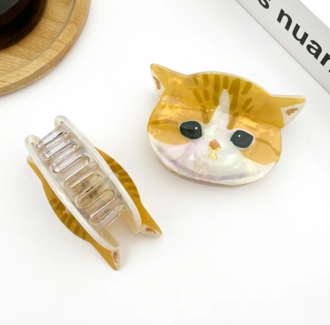A white acetate hair claw clip in the shape of a cute cat head with minimalist black line details for the face.