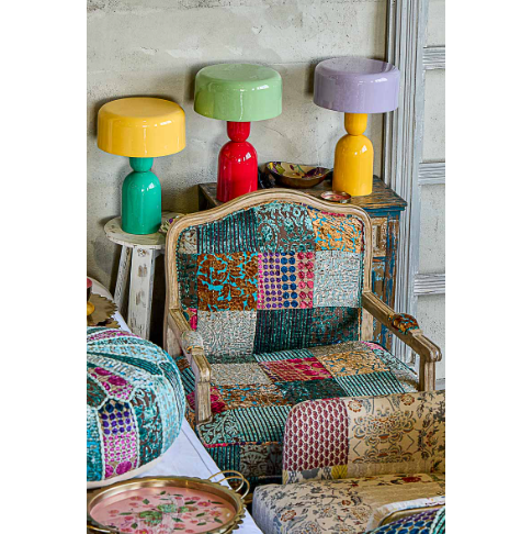 Several colorful, glossy modern table lamps in contrasting shades displayed on a rustic tabletop in a cozy, eclectic interior setting.