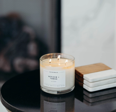 Style your side table with the lit Vetiver + Tonka 3-wick candle by Calyan Wax Co. displayed alongside modern wood and marble coasters.