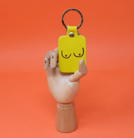 A unique and empowering bright yellow leather keyring shaped like a boob, a playful symbol of strength and femininity.