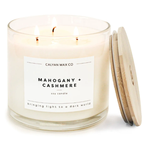 Create a cozy fireside atmosphere with the Mahogany + Cashmere 3-wick soy candle by Calyan Wax Co., featuring a clear glass tumbler and natural wooden lid.