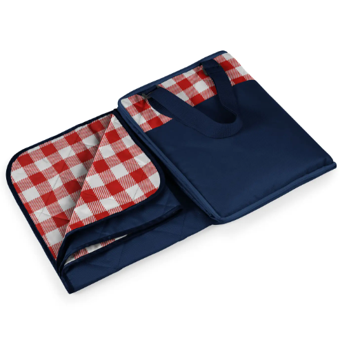 A folded picnic blanket in a navy blue tote with a red and white gingham pattern visible on the inside, with a small handles.