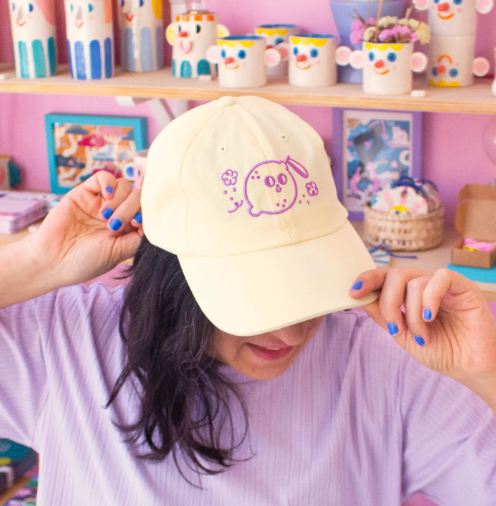 The Ana Seixas Magic Lemon Cap worn by model, showcasing how the light yellow cap with its purple "Magic Lemon" embroidery provides a stylish and comfortable fit.
