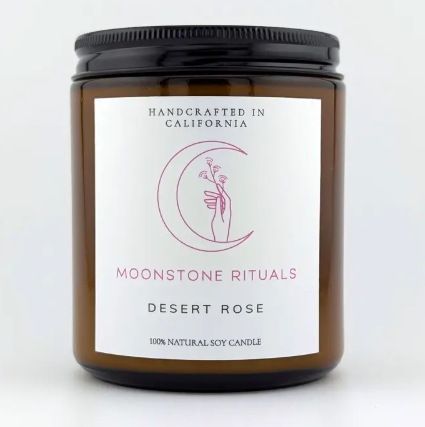 A Moonstone Rituals soy wax candle in a sleek glass jar with a minimalist label and a natural wooden wick in Desert Rose scent.