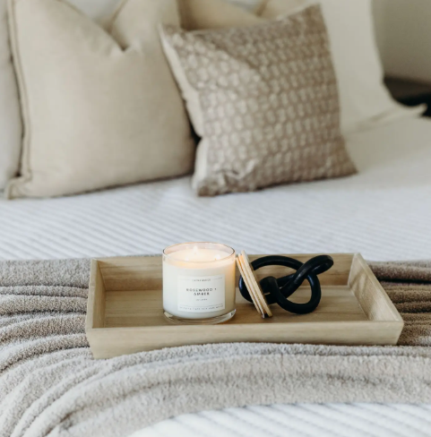 Style your bedroom tray with the lit Rosewood + Amber 3-wick candle by Calyan Wax Co. alongside neutral linens and decor.