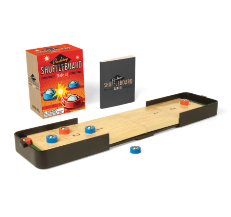 A miniature shuffleboard set with an extendable track, three red pucks, three blue pucks, and a black instructional mini book.