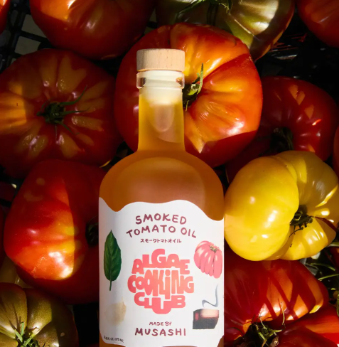 Showcase the limited-edition Musashi's Smoked Tomato Oil by Algae Cooking Club, artfully placed among a vibrant assortment of fresh, sun-ripened tomatoes.