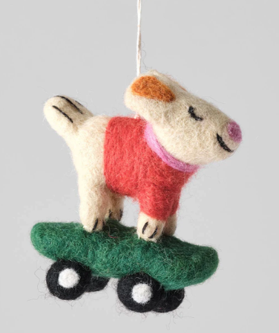 A felted wool ornament of a white and brown dog in a red sweater standing on a green skateboard.