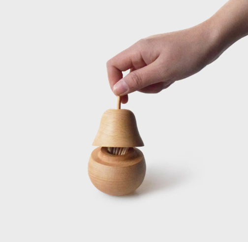 A hand demonstrating the functional design of the Senser Woodcraft Pear Toothpick Holder, revealing its interior capacity for toothpicks.