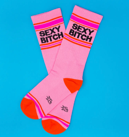 Close up of retro-style athletic socks featuring an orange contrast toe and heel with a bold block-letter "SEXY BITCH" statement.