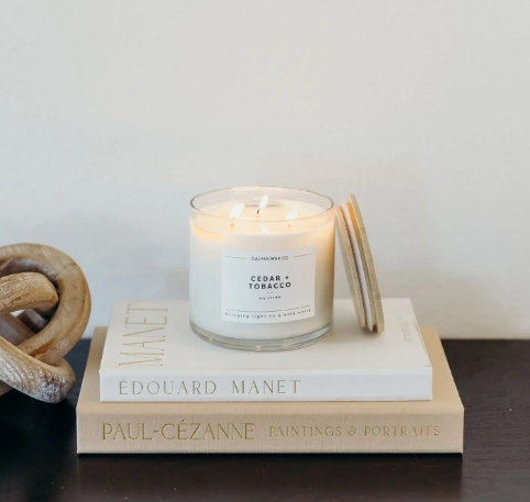 Style your coffee table or bookshelf with the lit Cedar + Tobacco 3-wick candle by Calyan Wax Co. stacked on art books.