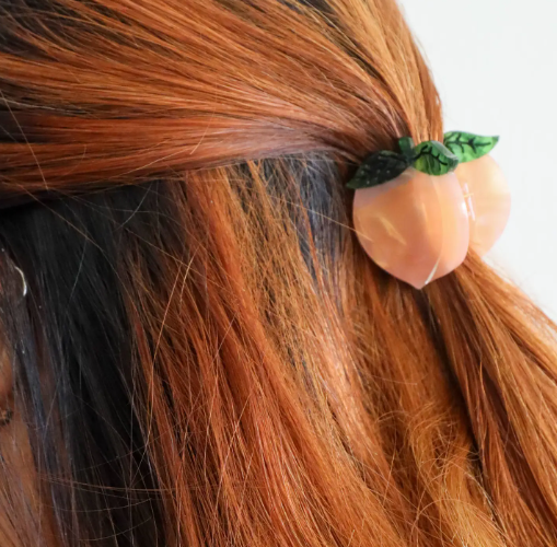 A close-up of a model with the Jenny Lemons Mini Peach Hair Claw, emphasizing its adorable scale and how it beautifully enhances summer hairstyles.