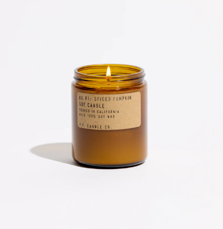 A lit amber jar soy candle radiating a warm, inviting glow and filling the room with a rich autumn fragrance.